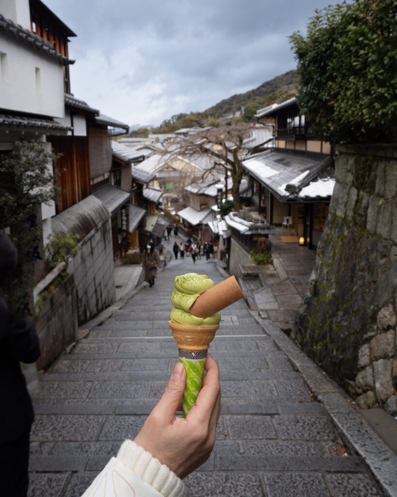 Hand Holding Green Tea Ice Cream Cone on Historic Japanese Street Wallpaper