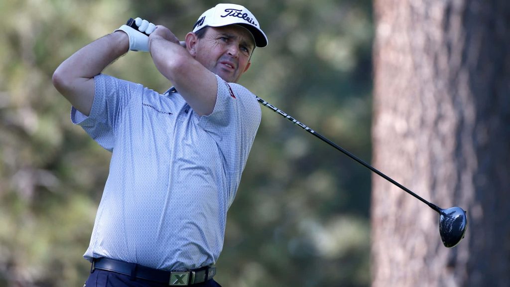Professional golfer Greg Chalmers mid swing in blue shirt and white cap on golf course fairway Wallpaper