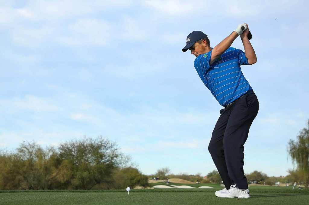 Left-handed golfer Greg Chalmers swings on tee box in blue polo golf wallpaper background