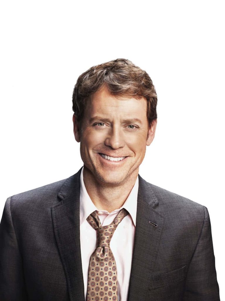 Portrait of actor Greg Kinnear smiling in suit and patterned tie on bright white background wallpaper