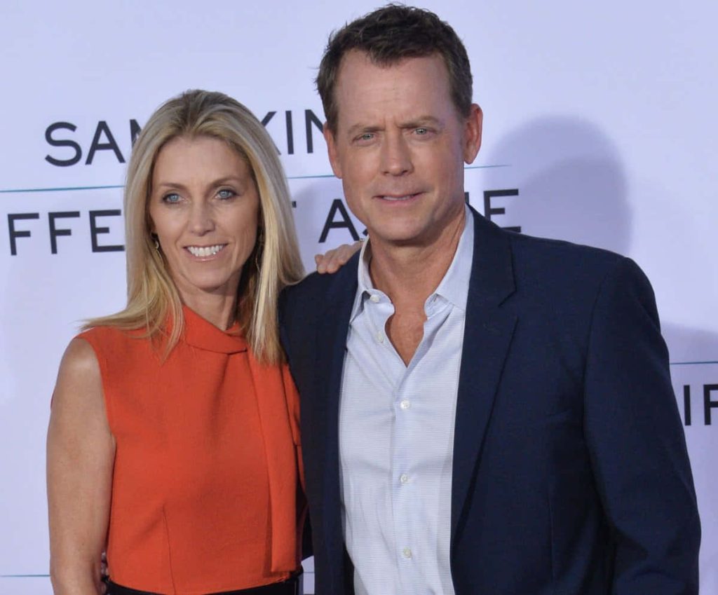 Actor Greg Kinnear in navy blazer with wife Helen Labdon in orange top posing on red carpet background Wallpaper