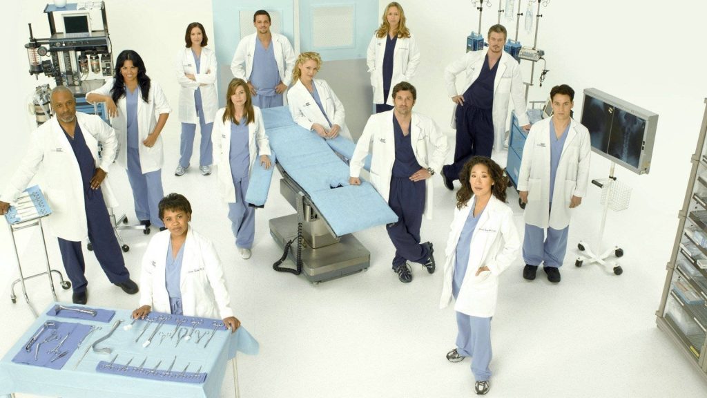 Grey's Anatomy promo wallpaper featuring cast in scrubs and lab coats in surgical room