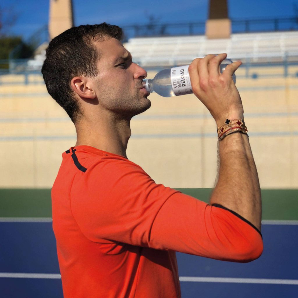 Grigor Dimitrov in orange shirt hydrating with Vitamin Well Reload on outdoor tennis court Wallpaper