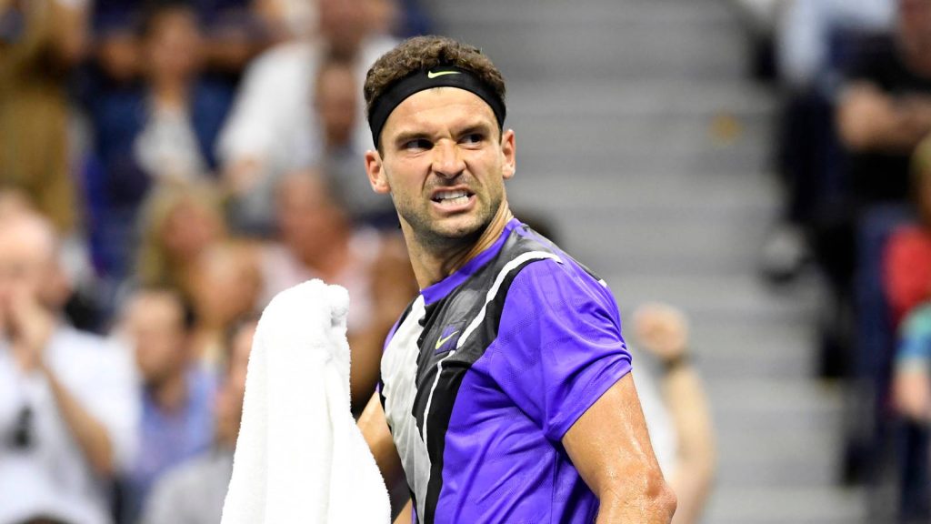 Grigor Dimitrov focused in purple Nike gear holding towel with blurred stadium tennis wallpaper