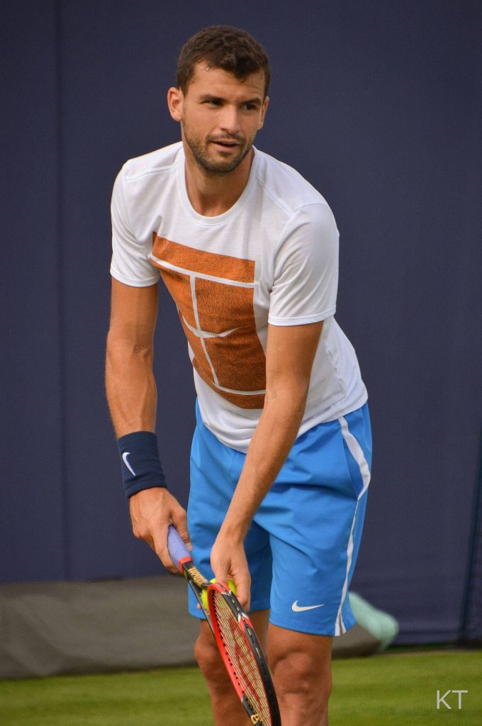 Grigor Dimitrov tennis player in white shirt and blue shorts grips racket on grass court wallpaper