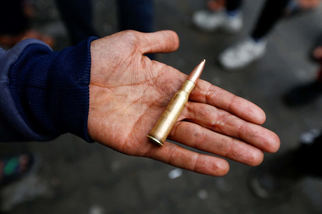 Close-up of weathered hand holding brass rifle bullet with blurred outdoor background wallpaper