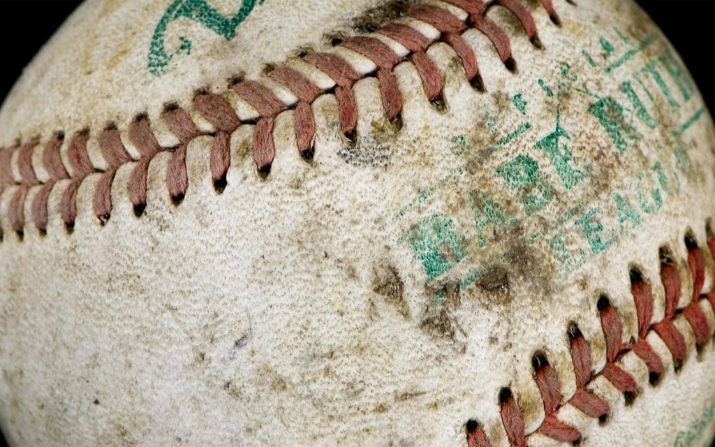 Close-up of weathered Babe Ruth League baseball with red stitching and textured scuffed leather Wallpaper