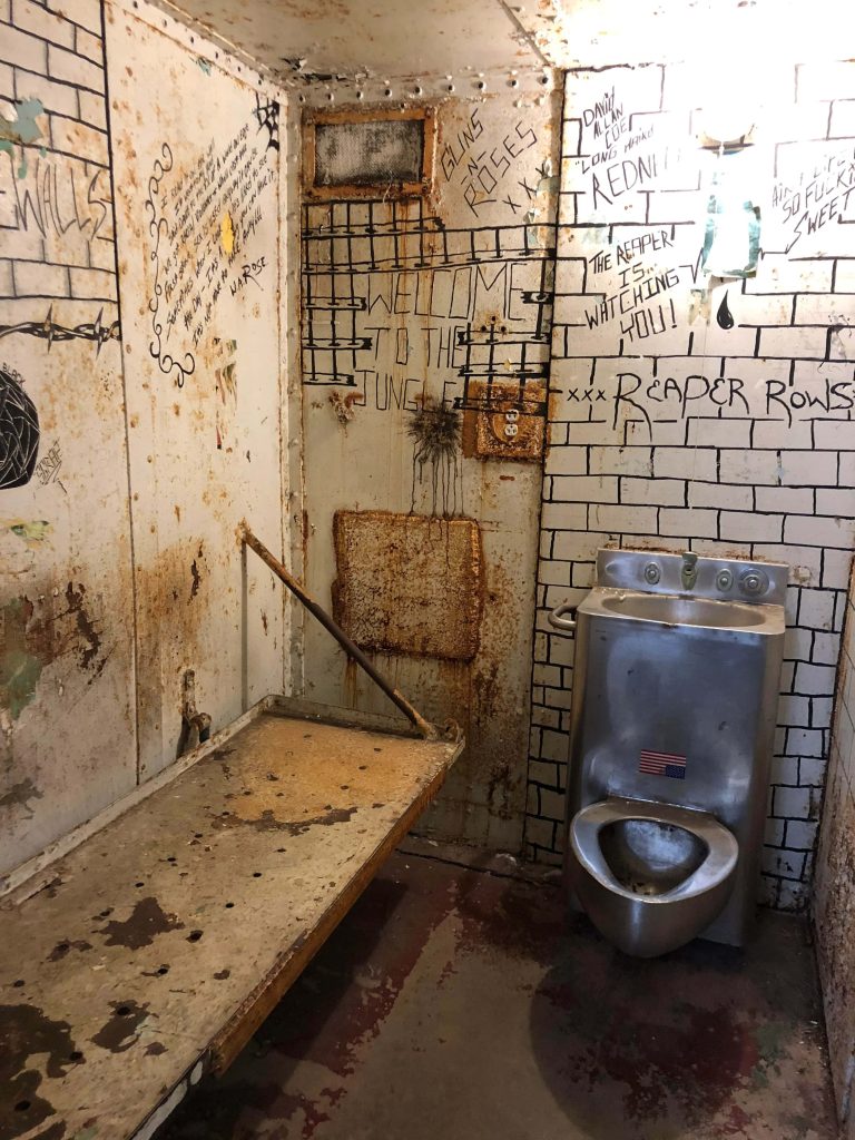 Derelict prison cell with rusted cot stainless steel toilet graffiti walls gritty jail wallpaper
