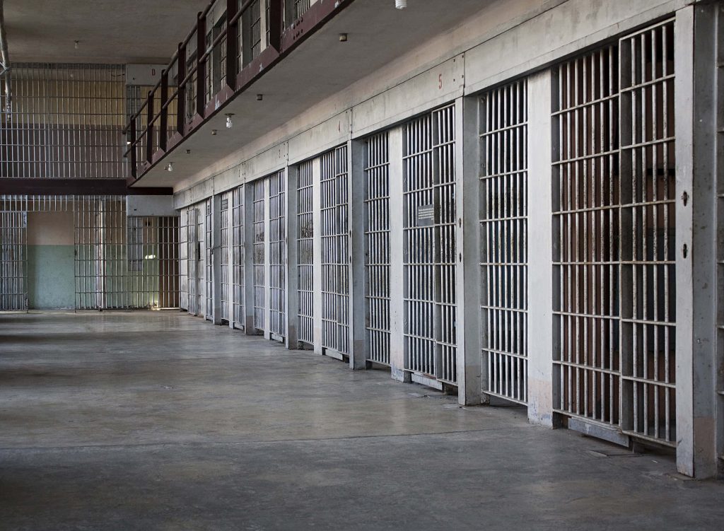 Prison cell block corridor with barred metal cells and concrete floor jail wallpaper background