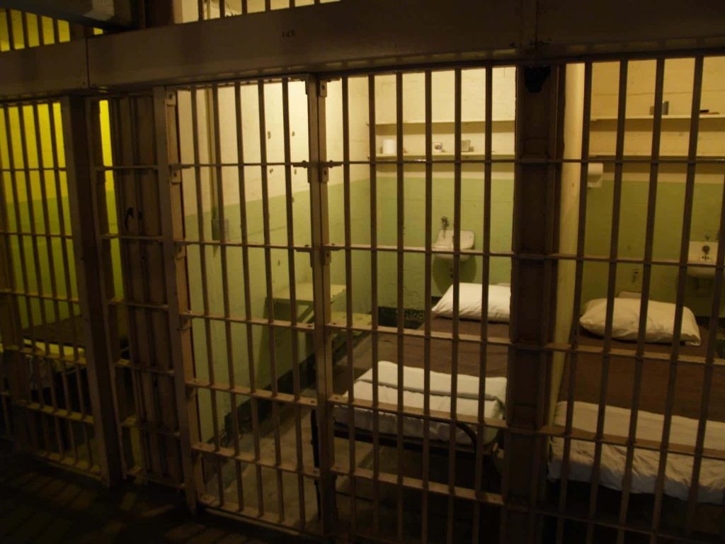 Gritty prison cell wallpaper behind iron bars dimly lit austere cots moody cinematic look