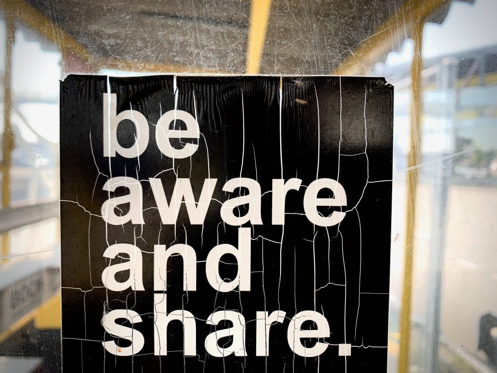 Close-up of gritty black sign with white Be Aware and Share text on cracked weathered surface background Wallpaper