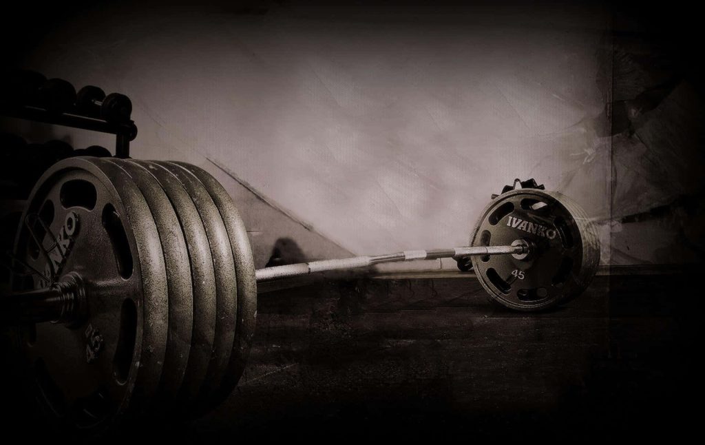 Barbell with 45lb Ivanko plates in moody gym setting gritty weight training wallpaper background