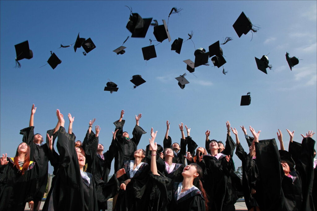 Joyful graduates in black gowns toss mortarboards skyward celebrating success and triumph Wallpaper