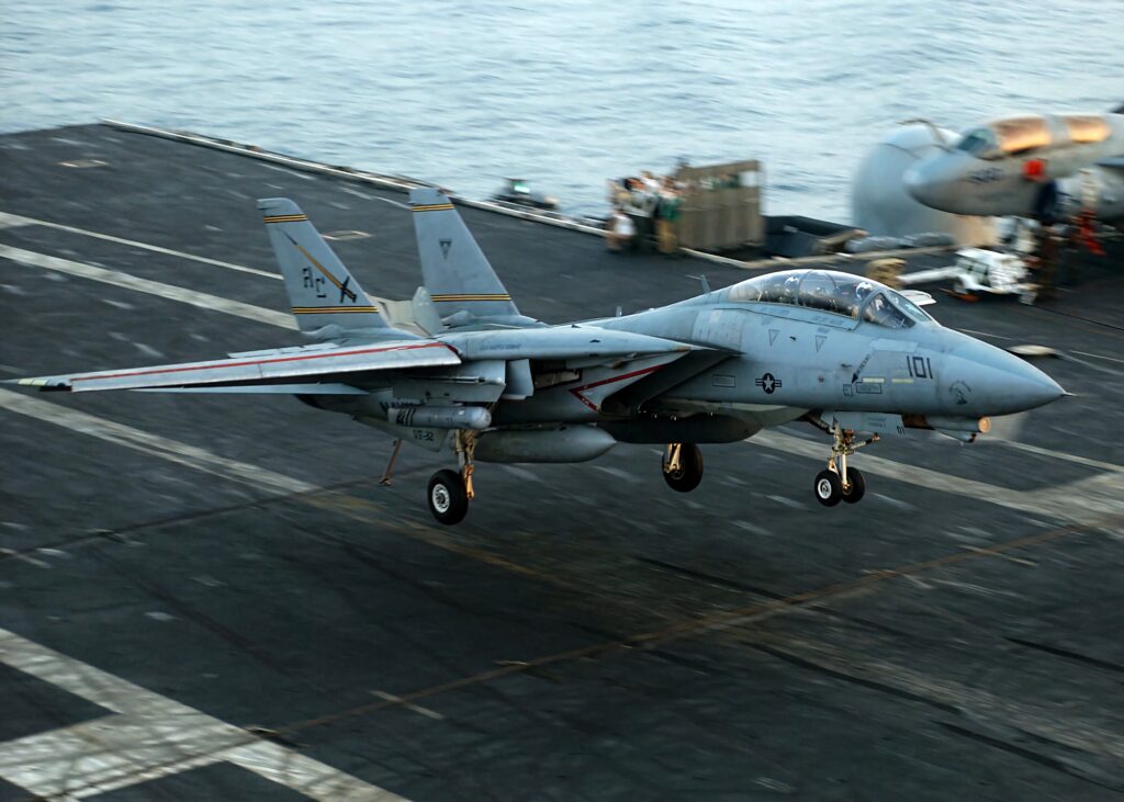Grumman F-14 Tomcat jet flying over aircraft carrier deck showcasing sleek wings and military markings Wallpaper