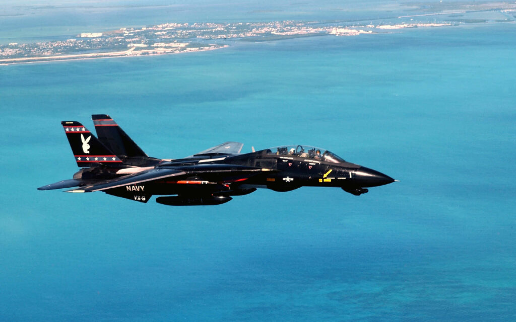 Grumman F-14 Tomcat fighter jet flies over turquoise waters with sleek black navy paint and sharp wings Wallpaper