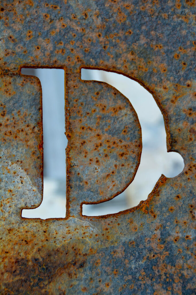 Letter D carved in rusted metal with industrial grunge texture and earthy tones wallpaper background