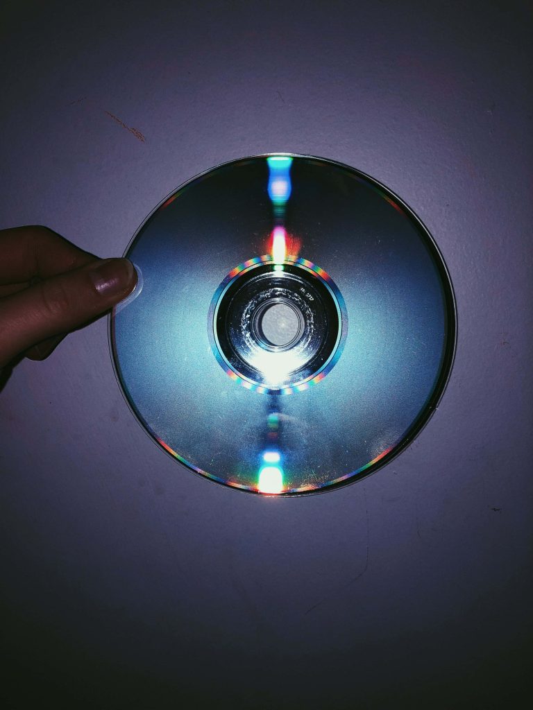 Hand holding compact disc with vibrant rainbow light on moody blue grunge retro wallpaper