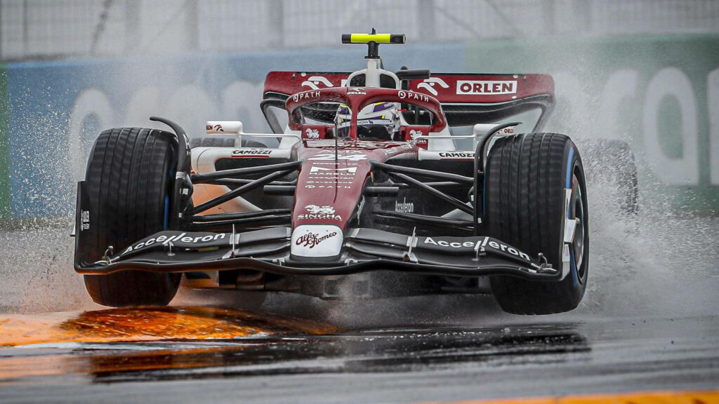 Guanyu Zhou driving Formula 1 car on wet rain-soaked track with dramatic water spray wallpaper