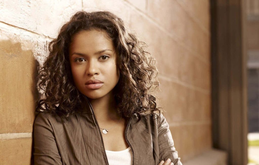 Portrait of actress Gugu Mbatha-Raw with curly hair against textured beige wall in soft lighting Wallpaper