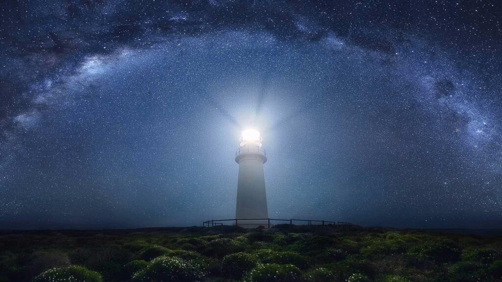 HD lighthouse wallpaper with Milky Way galaxy over coastal vegetation at night sky