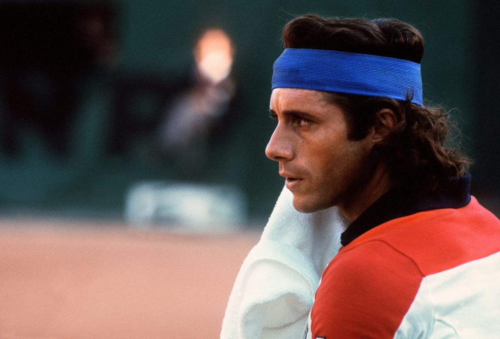 Tennis legend Guillermo Vilas focused on red clay court wearing blue headband vintage portrait wallpaper