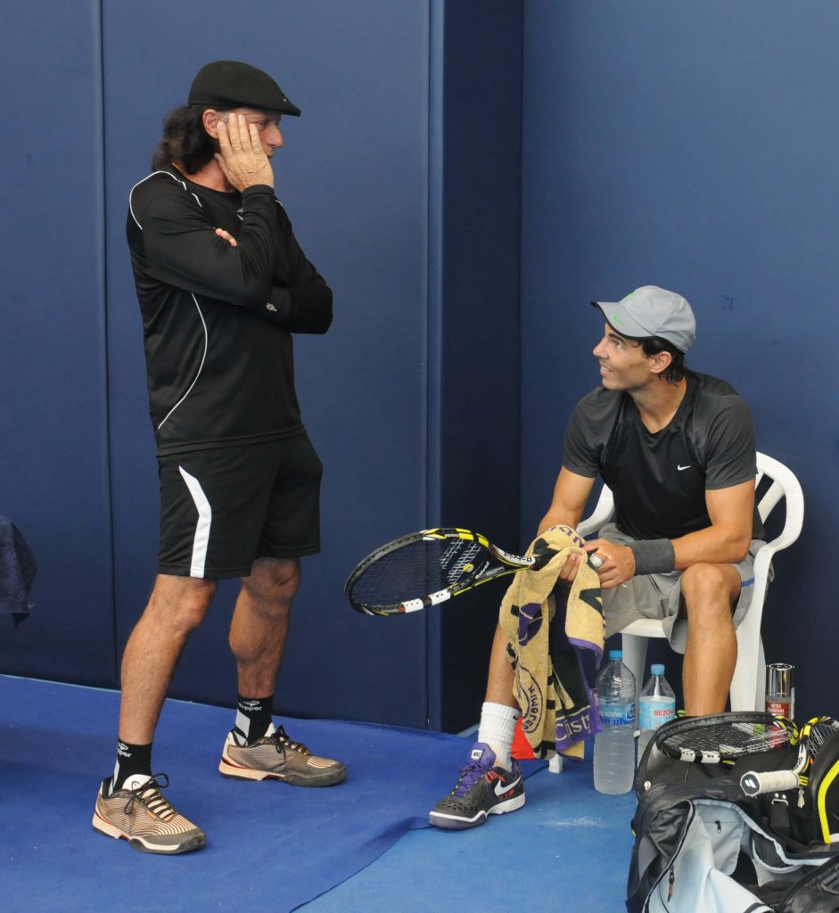 Guillermo Vilas and Rafael Nadal chatting on indoor blue tennis court in athletic gear Wallpaper