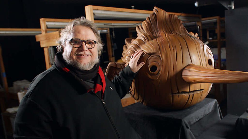 Guillermo del Toro with handcrafted wooden puppet head from Pinocchio stop motion film background Wallpaper
