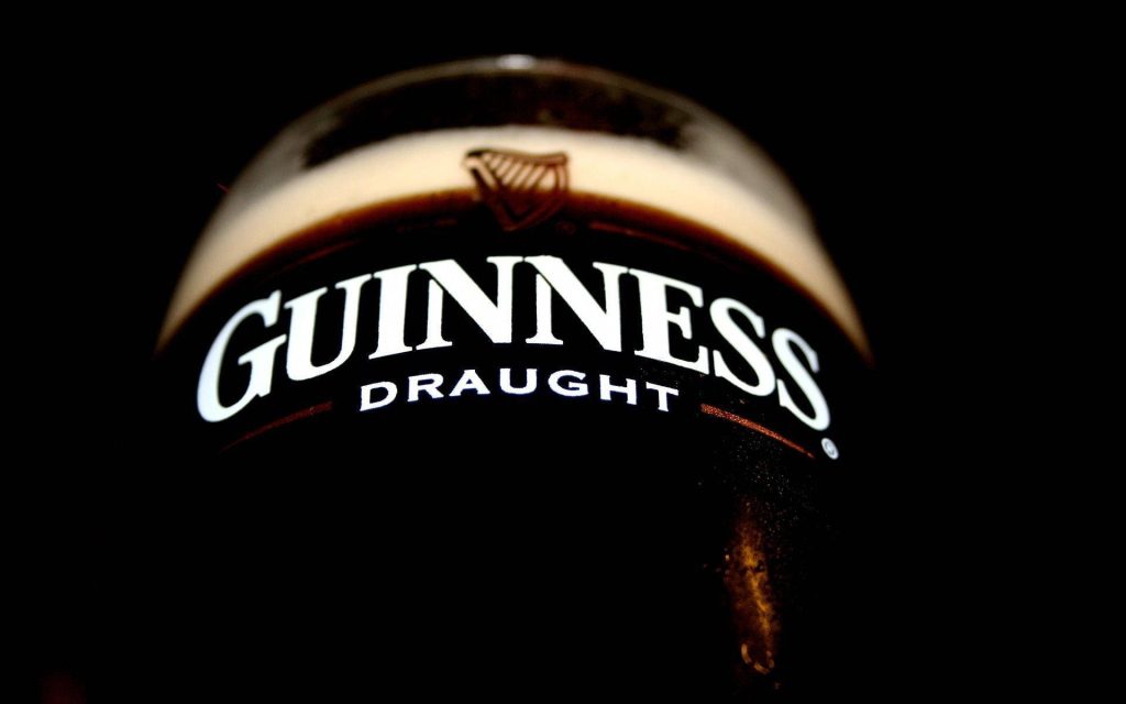 Low-angle Guinness Draught pint wallpaper with iconic white logo on dark moody background