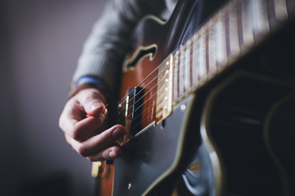 Close-up of musician's hand picking hollow-body electric guitar with warm tones and texture Wallpaper