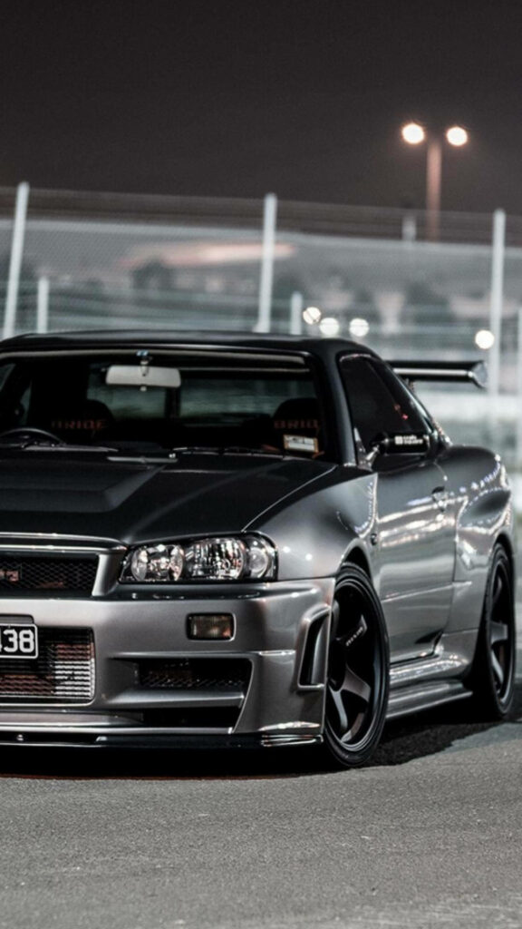 Gunmetal JDM car with bold body kit and large rear wing parked under vibrant city lights Wallpaper