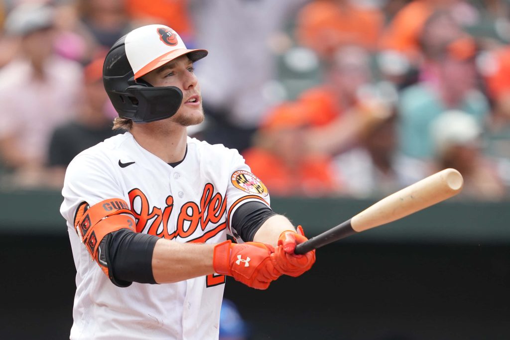 Baltimore Orioles Gunnar Henderson batting in white uniform vibrant orange accents stadium backdrop Wallpaper