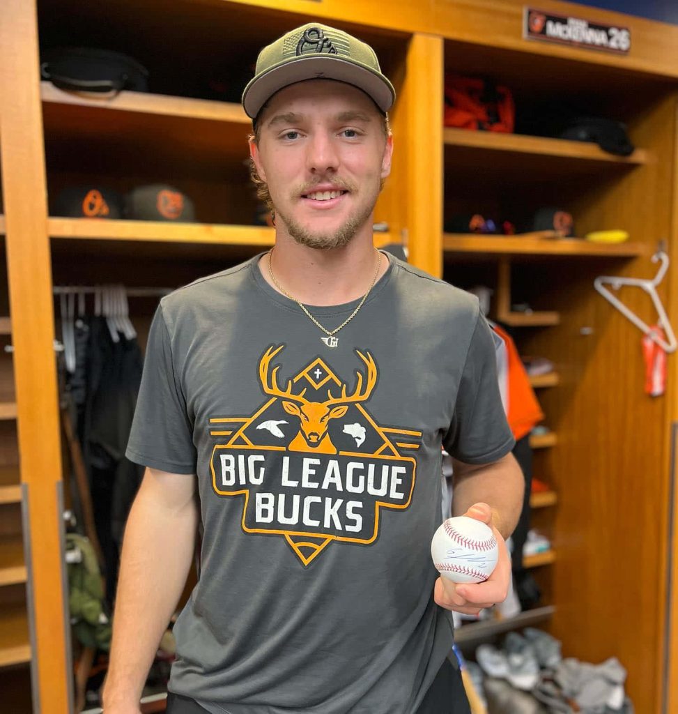 Baltimore Orioles shortstop Gunnar Henderson smiling in locker room wearing Big League Bucks tee Wallpaper