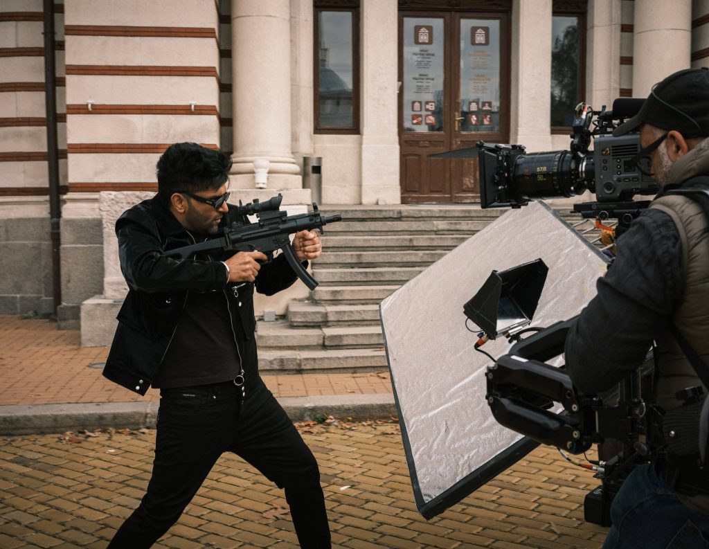 Guru Randhawa on set in black jacket holding submachine gun cinematic behind the scenes wallpaper