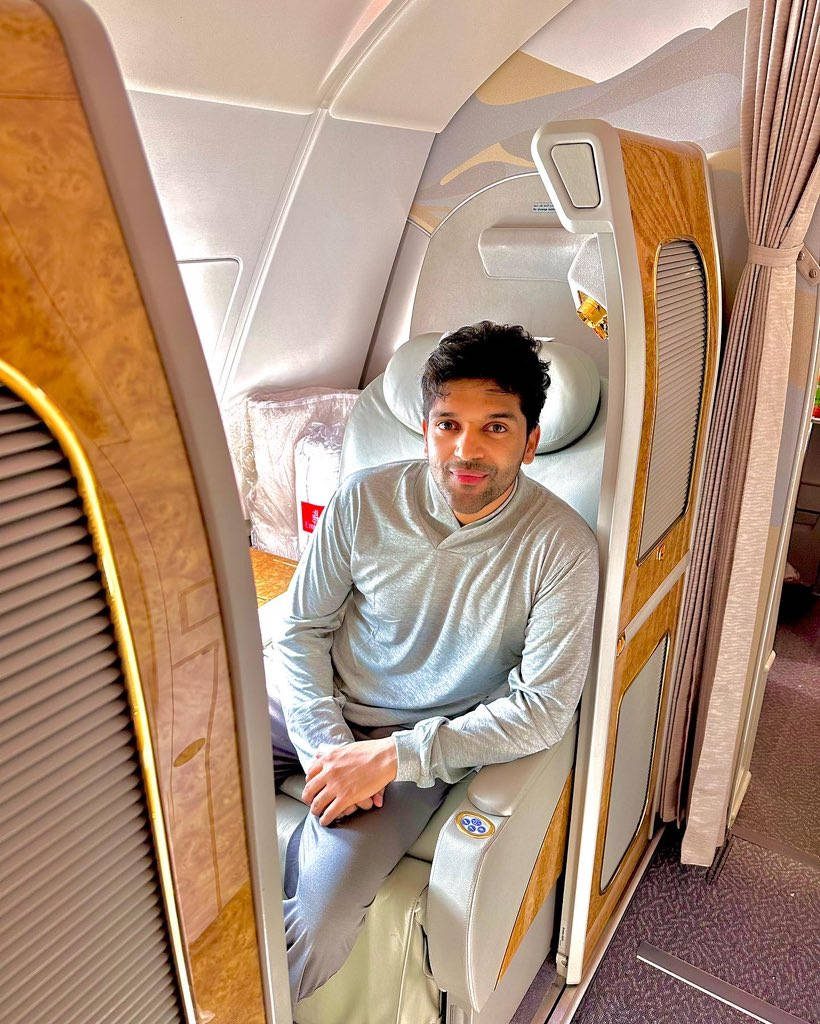 Guru Randhawa relaxed in luxury first-class airplane suite with wood accents and cream upholstery Wallpaper