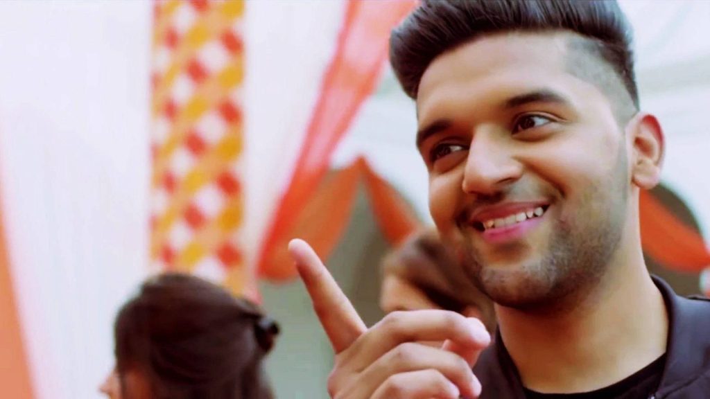 Guru Randhawa smiling and pointing up vibrant close-up wallpaper with soft lighting background