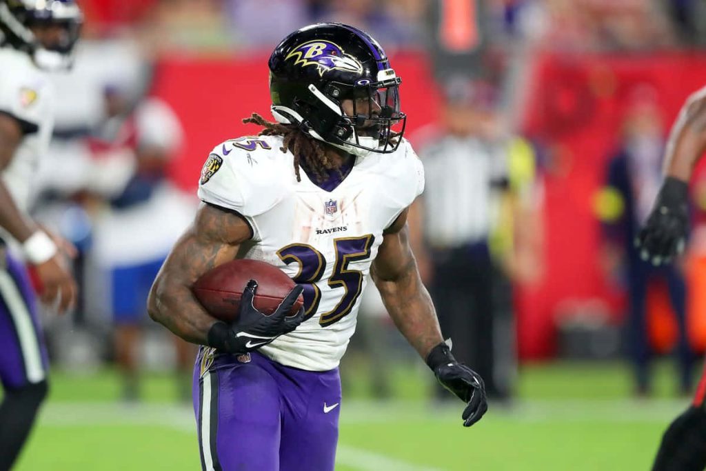 NFL running back Gus Edwards in Baltimore Ravens white jersey charging with football action shot Wallpaper
