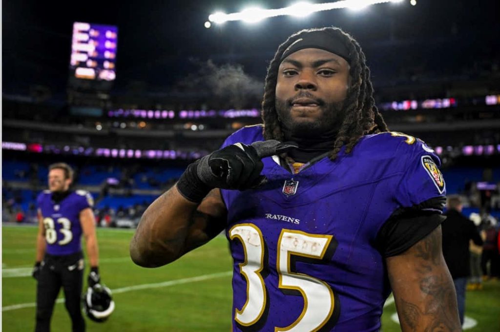 Gus Edwards Baltimore Ravens #35 celebrating in cold weather with vibrant purple stadium lights background Wallpaper