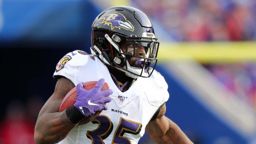 Dynamic action shot of Gus Edwards Ravens running back in white jersey sprinting forward Wallpaper