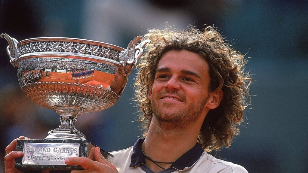 Tennis legend Gustavo Kuerten holding silver Roland Garros trophy with joyful smile wallpaper
