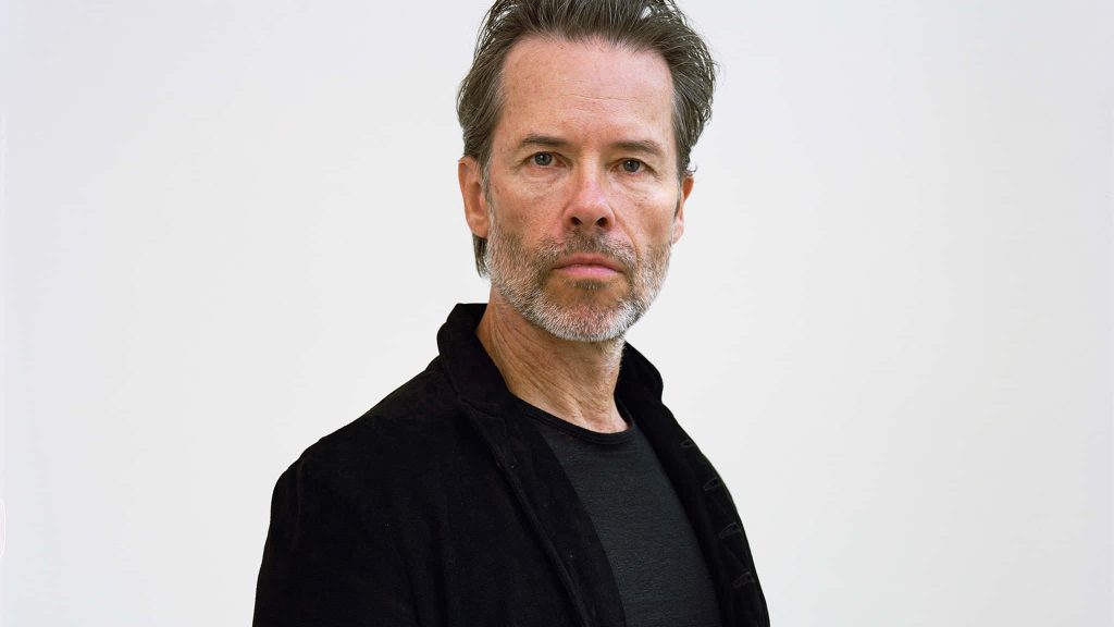 Close-up portrait of actor Guy Pearce in black jacket with intense expression on white background Wallpaper