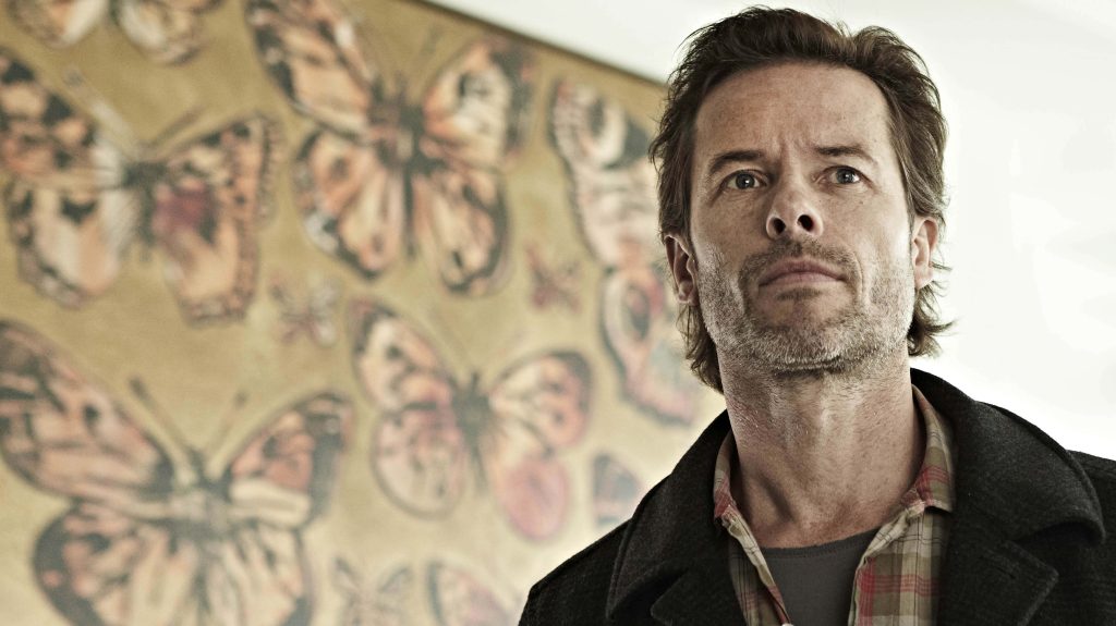Guy Pearce contemplative portrait wallpaper in plaid shirt dark coat warm butterfly background