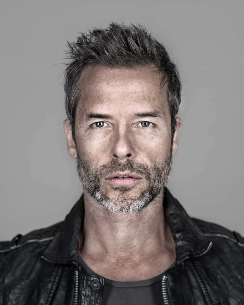 Professional portrait of actor Guy Pearce in black leather jacket with piercing gaze and beard Wallpaper