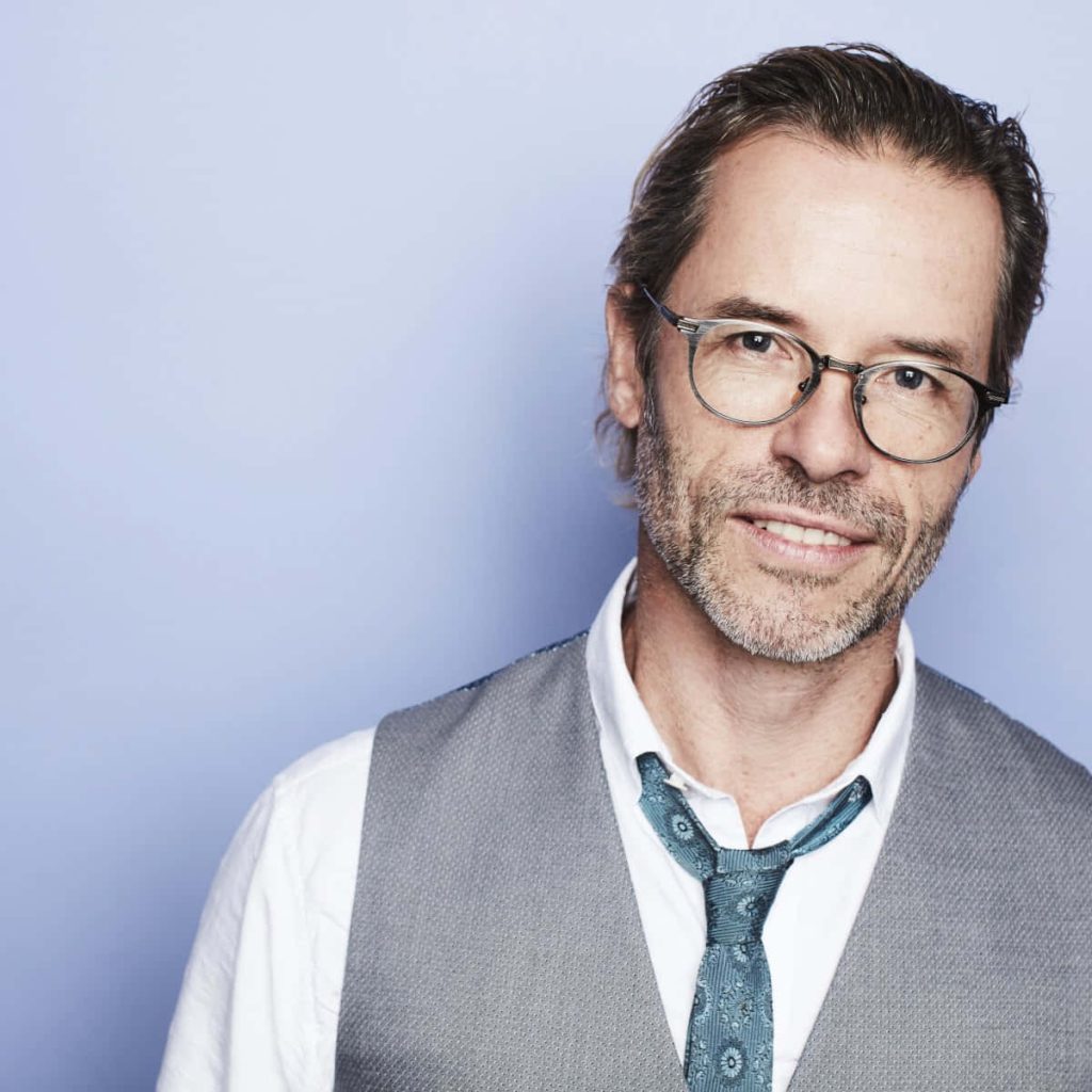Portrait of award-winning actor Guy Pearce in white shirt grey vest tie and glasses on blue background Wallpaper