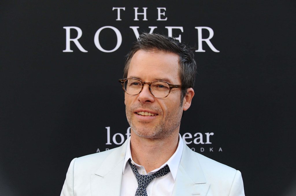 Guy Pearce in white blazer and tortoiseshell glasses smiling on red carpet for The Rover film Wallpaper