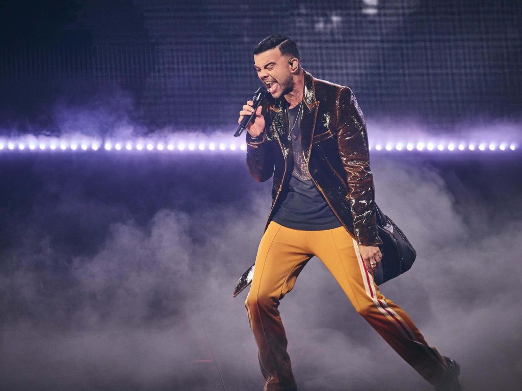 Guy Sebastian performing live in metallic blazer yellow pants purple stage fog concert wallpaper background