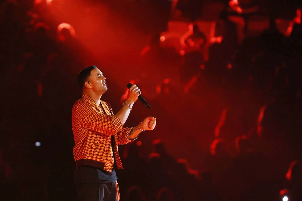 Guy Sebastian performing live in orange jacket under red stage lights concert wallpaper background