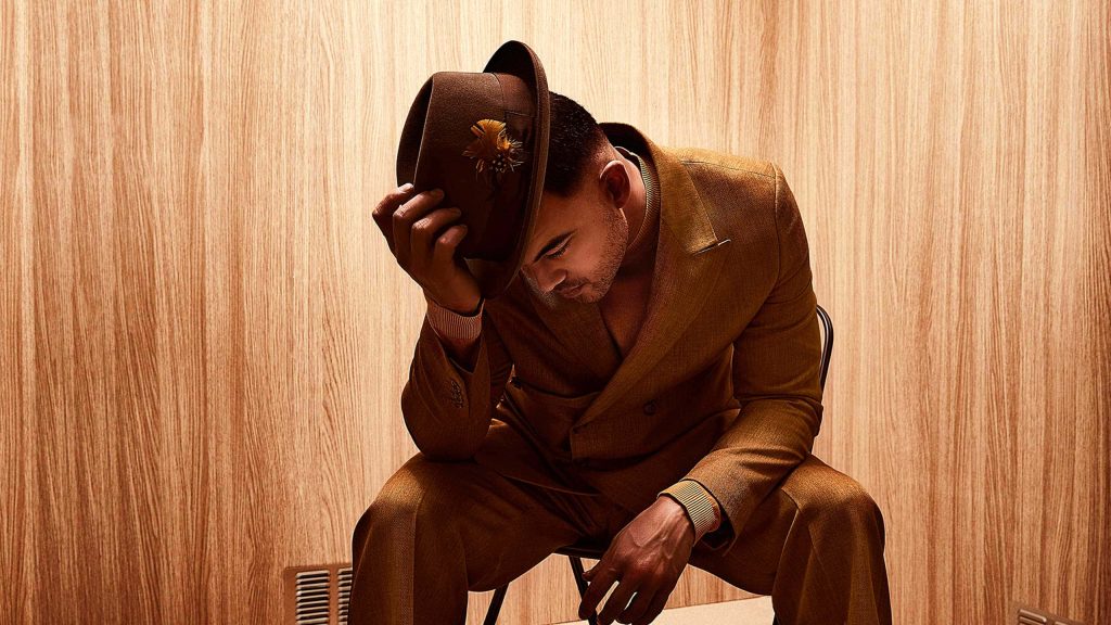 Guy Sebastian in tailored brown suit and fedora soulful monochrome portrait wood-paneled background Wallpaper