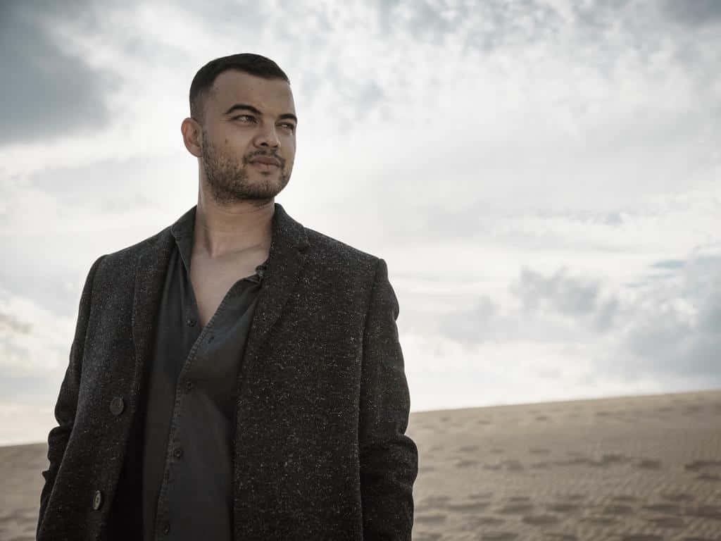Guy Sebastian portrait in dark blazer on sandy landscape under overcast sky calm mood wallpaper