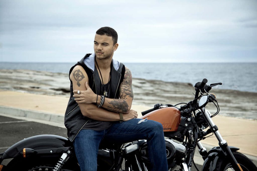 Guy Sebastian on motorcycle with tattoos sleeveless hoodie moody coastal background wallpaper