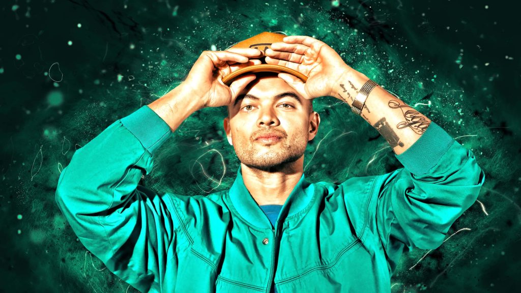 Portrait of Australian artist Guy Sebastian in teal bomber jacket and cap on green background Wallpaper